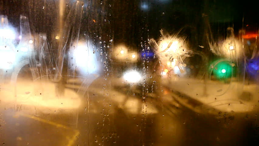 Tram's rear window view. Tram turns right and passes over switch.  Cold weather cityscape. Night time. Focus on window. Glowing blurred lights. 