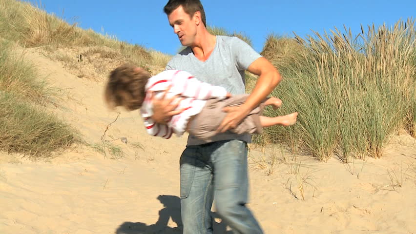 Young father with his cute son playing  together in sand dunes by the coast  filmed at 60FPS