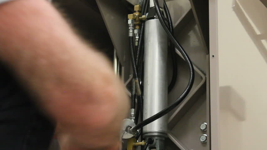 Biomedical technician tightens hoses, nuts, on hydraulic cylinder he installed in medical treatment table.  