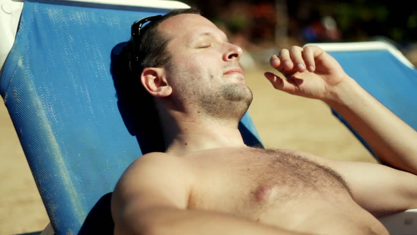 Young handsome man lying on blue sunbed and taking sunbath  