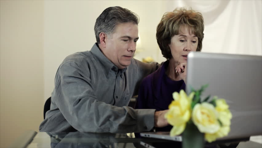A mature couple searching or the internet on their wireless laptop computer smile and converse about something they see.