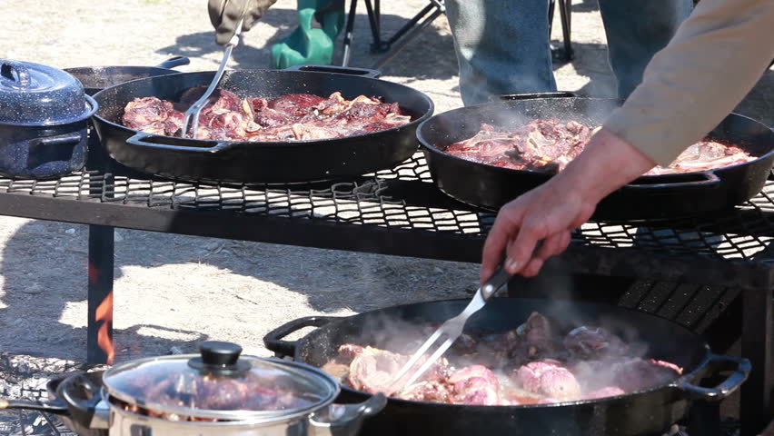 Meat Mutton lamb steaks and chops cooking in cast iron pans over an open outdoor fire. Cowboy and sheep camp bbq and party. Fresh meat with smoke and oil boiling near Dutch Oven.