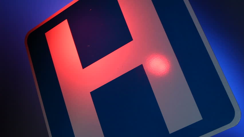 A close up of a hospital sign with flashing red and blue lights reflected on the sign