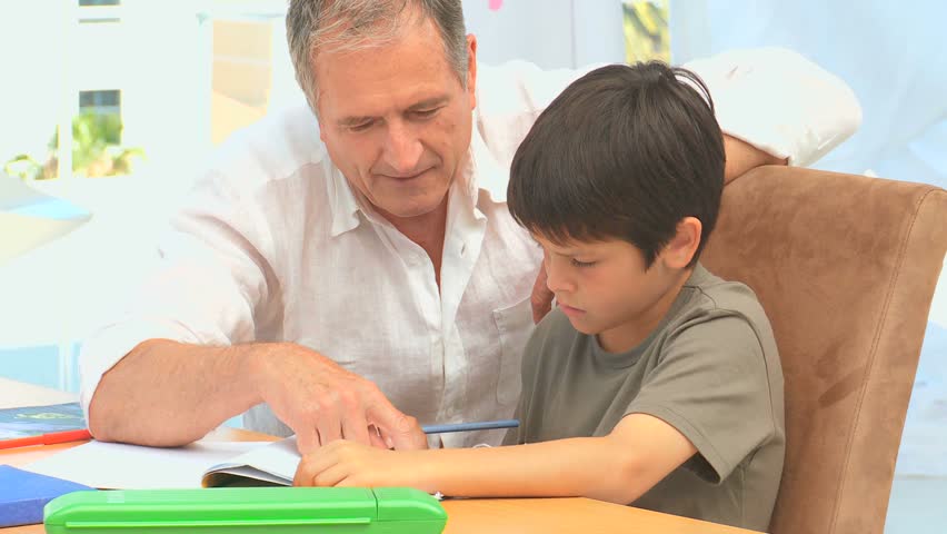 Grandfather helping his grandson to do his maths homeworks on a table