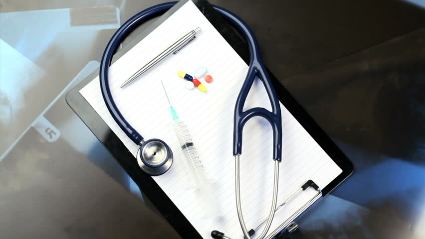 Stethoscope, pills, glasses and a pen turning with a blue and black background