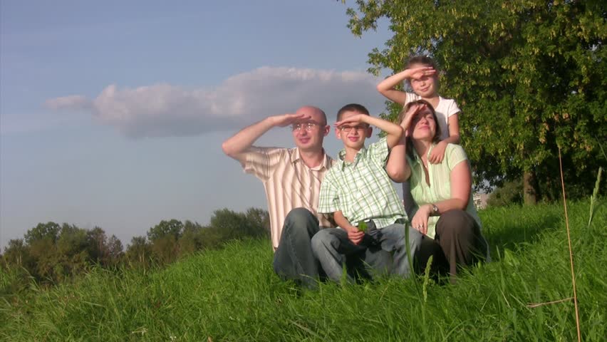 Family with two children sits in a grass and looks afar. Summer day.