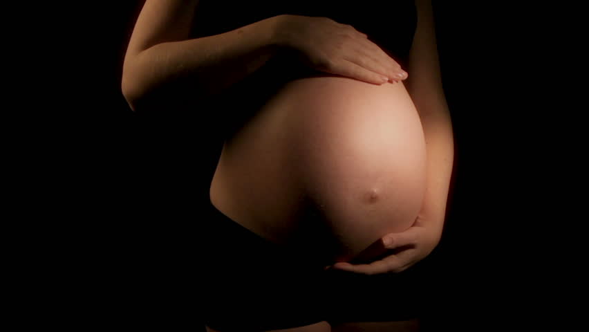 Pregnant woman strokes tummy (HD) Dolly shot of pregnant woman's belly on dark background. Shot in full progressive High Definition.