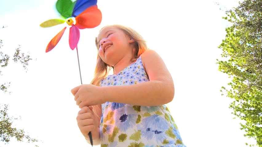 Cute little blonde girl happy playing with a toy pin wheel outdoors