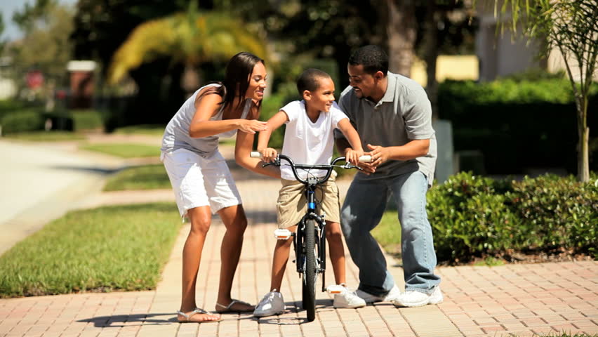 Cute young african-american boy being encouraged by his parents as he practices riding his bicycle