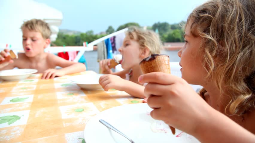 Three kids are sitting at balcony and eating ice cream in waffles