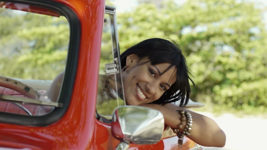 young adult brunette woman driving convertible red car and looking at camera
