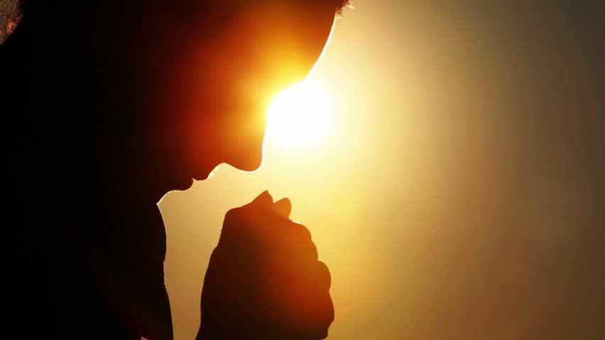 Silhouette of woman head with sunshine behind, holding two fists together and bowed head, after rises head up