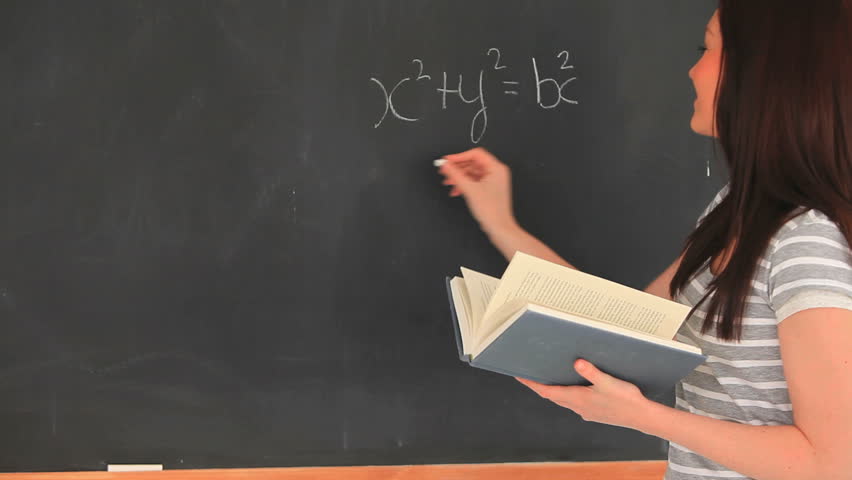 Beautiful woman writing a mathematical formula on a blackboard in a classroom
