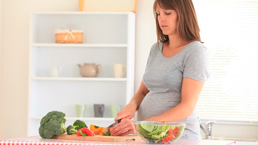 Pregnant woman preparing vegetables in her kitchen