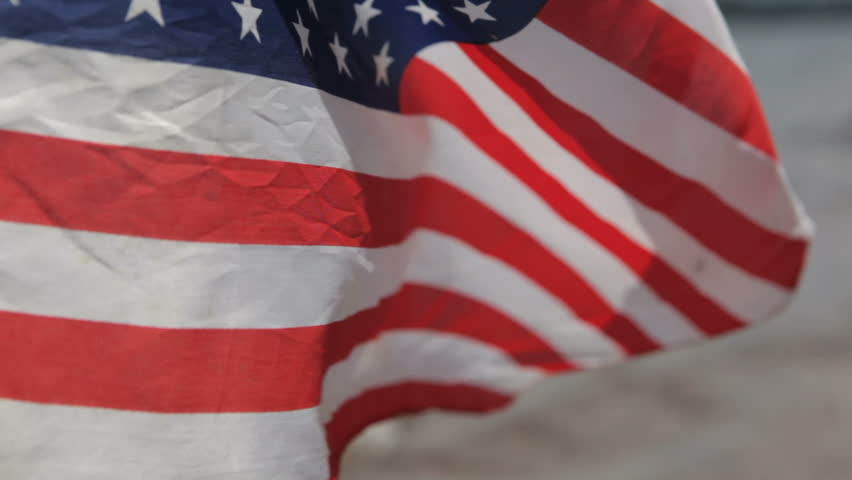 a US flag flapping in a gusty wind with a lake in the background