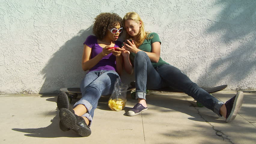 Two women friends sitting on skateboards