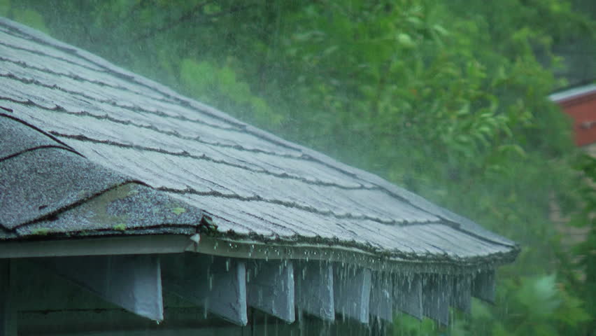 Heavy rain falling on the edge of a roof.