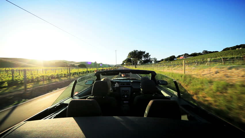 Visitors driving an open top car through the wine region of Napa Valley as the sun sets