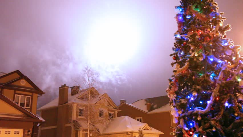Salute in night sky over houses and christmas fir-tree