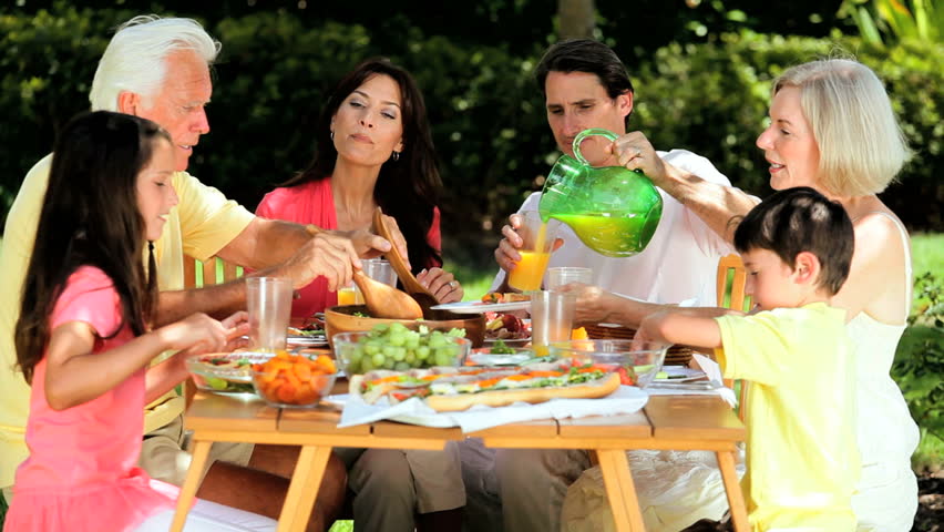 Three generations of caucasian family sitting outdoors sharing a healthy lunch together