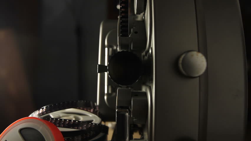 Includes two shots. Looking into the lens of an antique 8mm film projector as it is turned on and projecting beams of light. Includes projector audio.