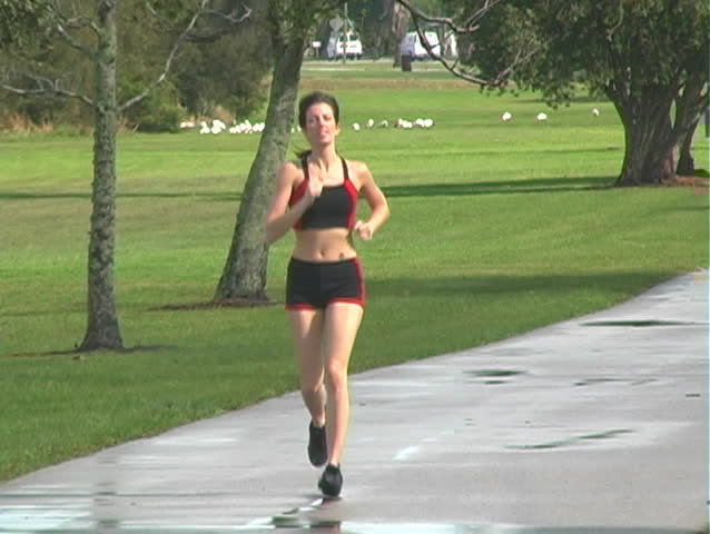 A beautiful young woman jogging outdoors toward the camera (full-length)