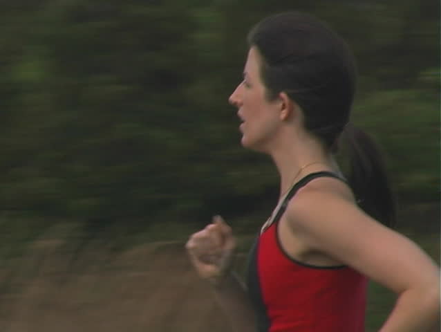 A beautiful young woman jogging outdoors.  Camera pans left to follow.