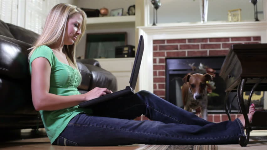 A happy little Jack-Rat Terrier dog joins his pretty owner while she sits on the floor working on her laptop. Slight camera tracking motion