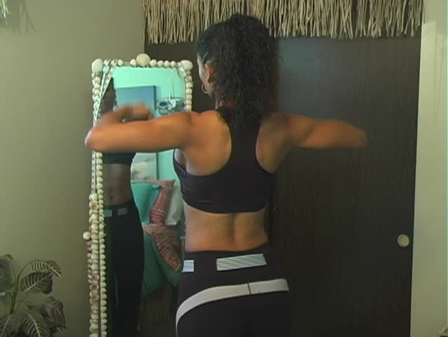 A beautiful woman with remarkable muscle definition checks her fitness and weight loss progress in front of a full-length mirror.