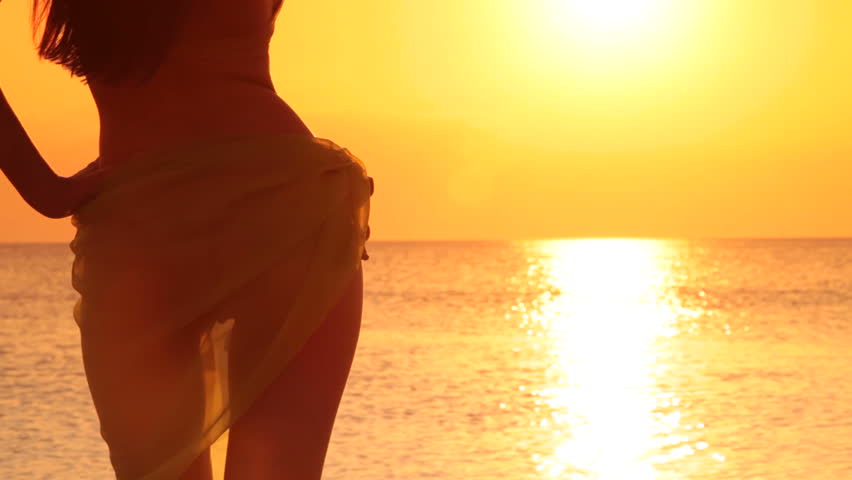 unrecognizable Woman in the pareo  looking at the sunset by the sea