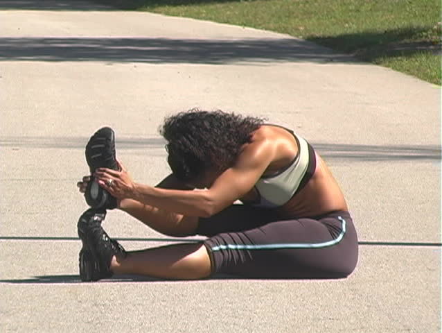 A beautiful woman stretches her legs on a jogging track before running on a bright, sunny day.