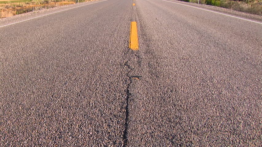 A two lane blacktop highway slices through mountains.