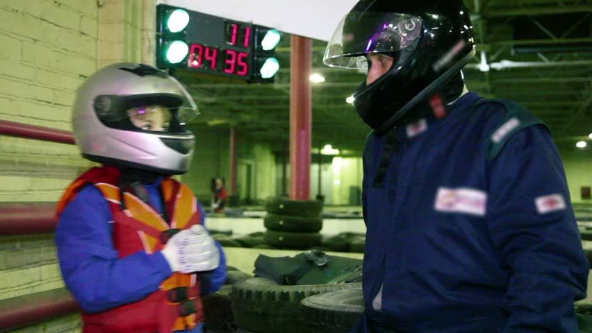 Boy and trainer in racing helmets hit his fists into hand, at ground for carting 