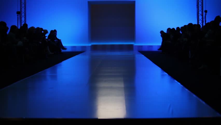 Many people are waiting for beginning of fashion show, sitting in dark, upward motion