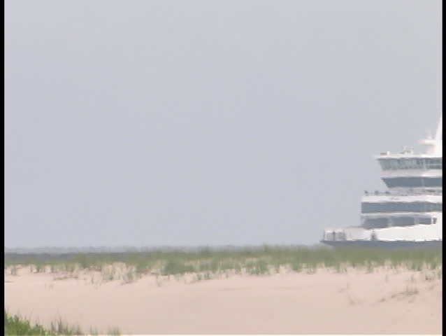 A passenger boat passes by a sandy coastline.
