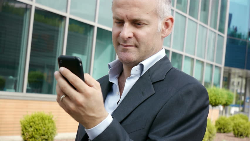 Portrait of happy businessman with mobile telephone, smart phone, typing and browsing the internet and looking at camera