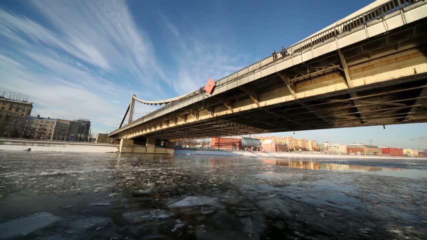 Ship sails under Crimean bridge and move to other side, houses and traffic on city waterfront 
