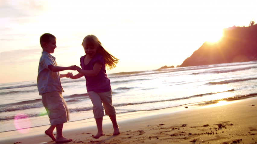 Grandparents and grandchildren enjoy a day at the beach.  Their activities include using a computer, walking on the beach, watching the sunset, having a drink, holding hands, and sharing an embrace.