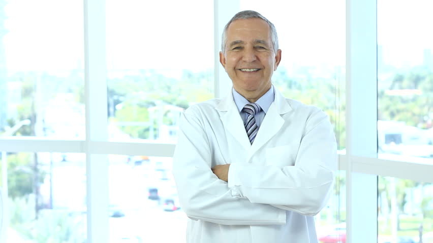 Senior male doctor walks into frame, crosses arms and nods, he is smiling