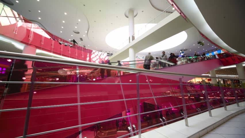 Many peoples move on escalators in multiple floors shopping center, border illumination change light color