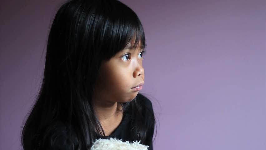 A cute little upset Asian girl is comforted by her teddy bear.