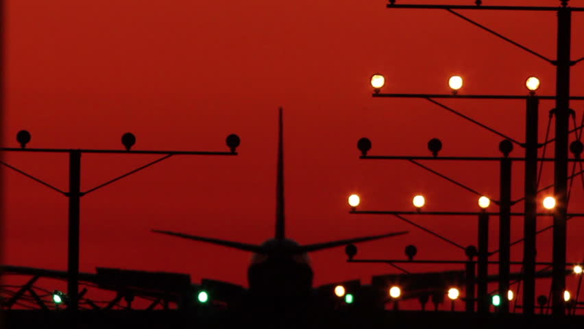HD footage of a twin engine jet plane landing in silhouette against a red sky with visible atmospheric distortion.  Jet engine audio included
