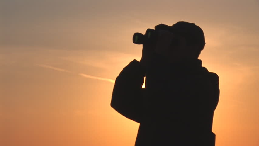 young man looking through binoculars at sunset