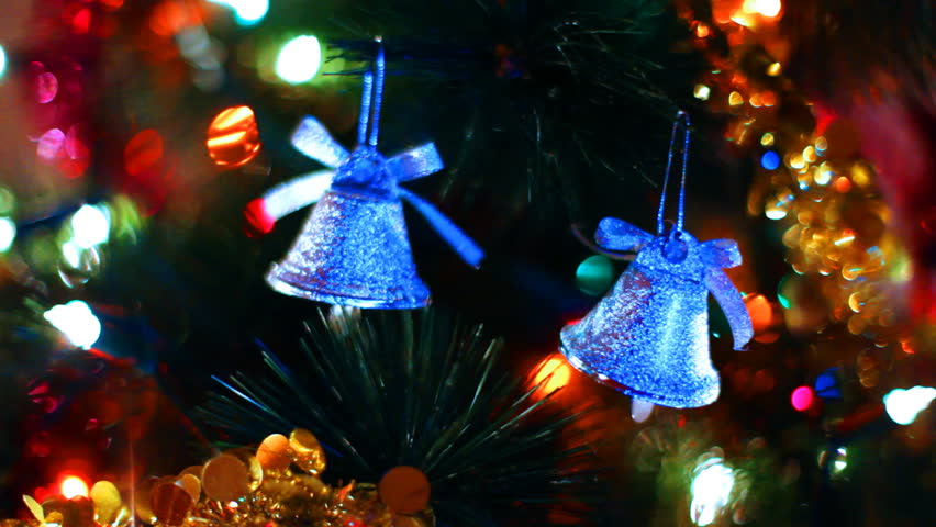 two blue toy bells hang on Christmas tree among of blinking colored garlands, close-up