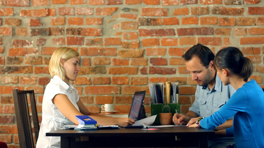 Real estate agent signing contract and giving keys to young couple
