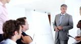 Mature male leader giving presentation through graph to team in meeting
