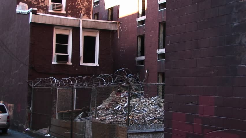 A cyclone fence and barbed-wire should prevent unwanted visitors from accessing an air-conditioner that still sits in a window of an abandoned building.