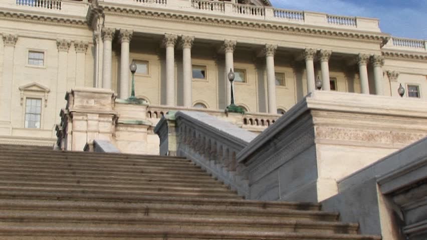 Camera pans up from steps of U.S. Capitol building in Washington, DC, to its landmark dome and cast-iron Freedom statue on top.