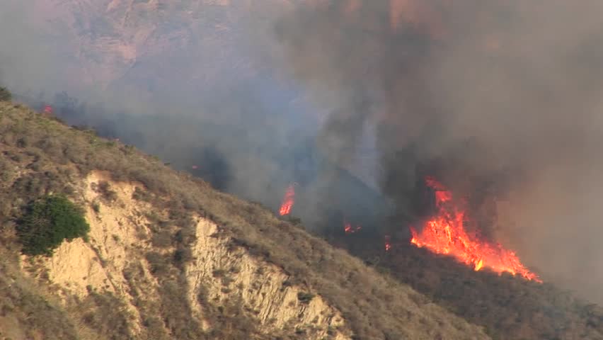 Zoom-out from wildfires burning on a smoky hillside in southern California.