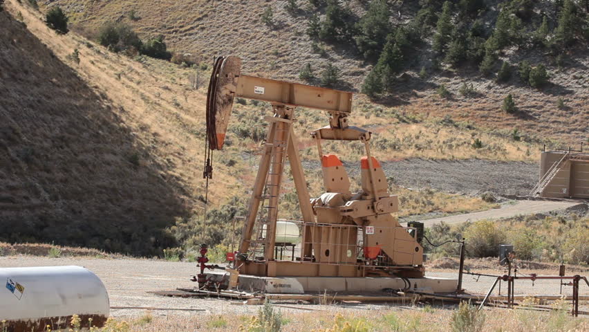 Oil well pumping crude from deep valley between mountains in central Utah. Propane motor powers the pump that extracts the oil. Fast motion timelapse.
